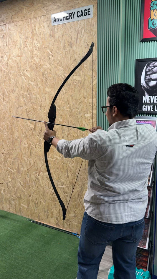 A person aims a bow and arrow in an archery cage.
