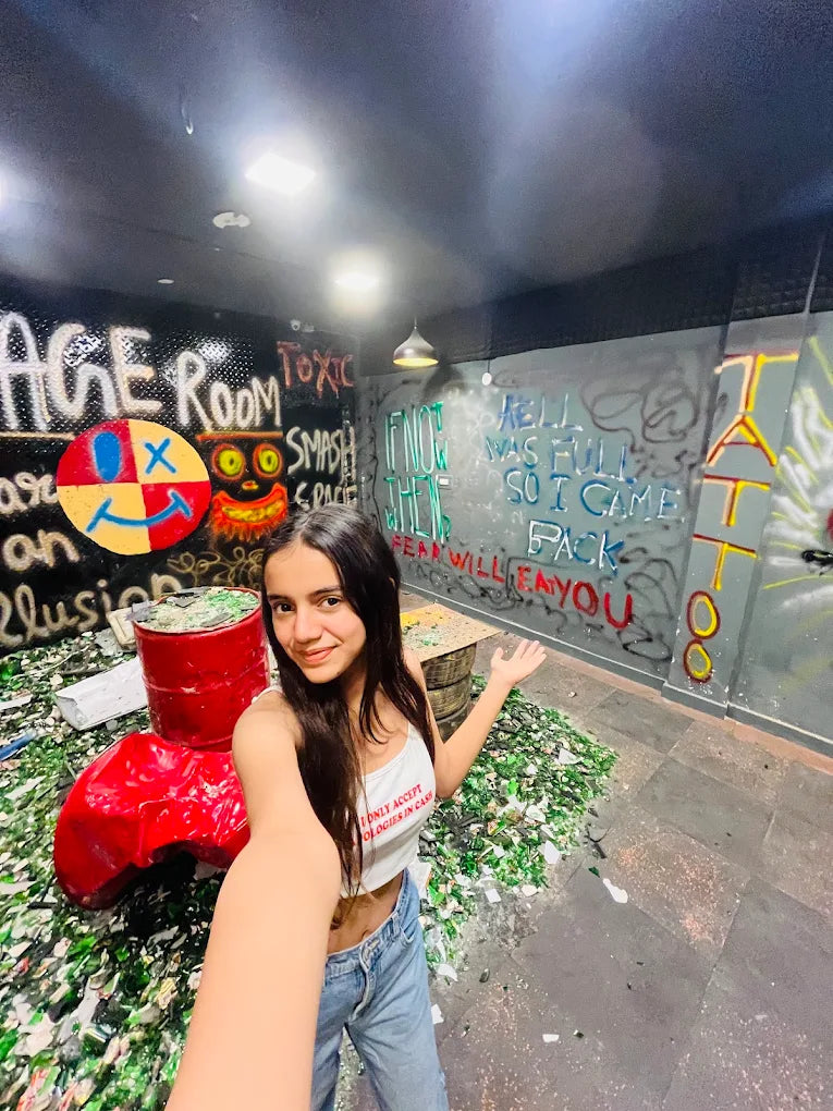 A young woman poses in a room filled with broken glass, surrounded by graffiti.