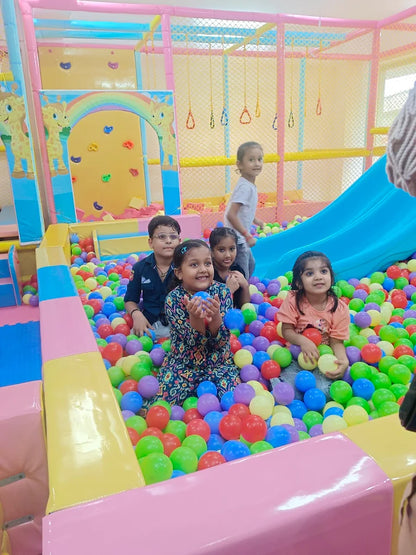 Children play in a colorful ball pit with a slide in the background.