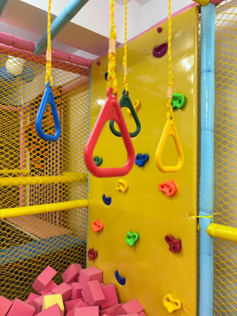 Children's indoor playground with a climbing wall, hanging rings, and foam blocks.
