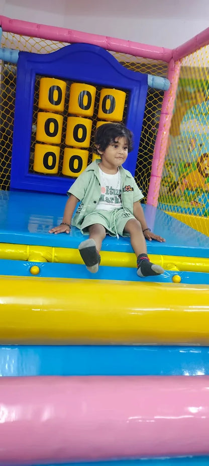 A young child sits on a colorful inflatable playground structure. The child is wearing a light green outfit and grey socks.