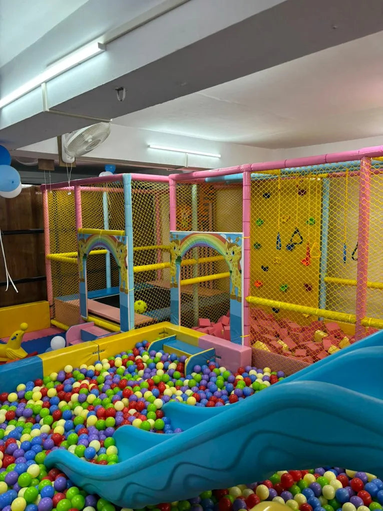 A colorful indoor playground with a ball pit, slide, and climbing wall for children.