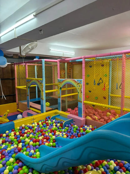 A colorful indoor playground with a ball pit, slide, and climbing wall for children.
