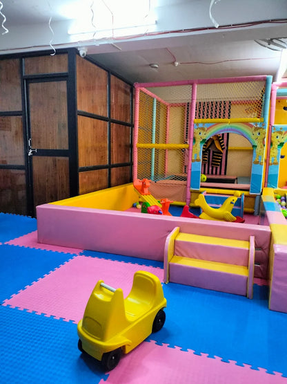 A brightly colored indoor playground with soft mats, a ball pit, and a yellow ride-on toy for young children.