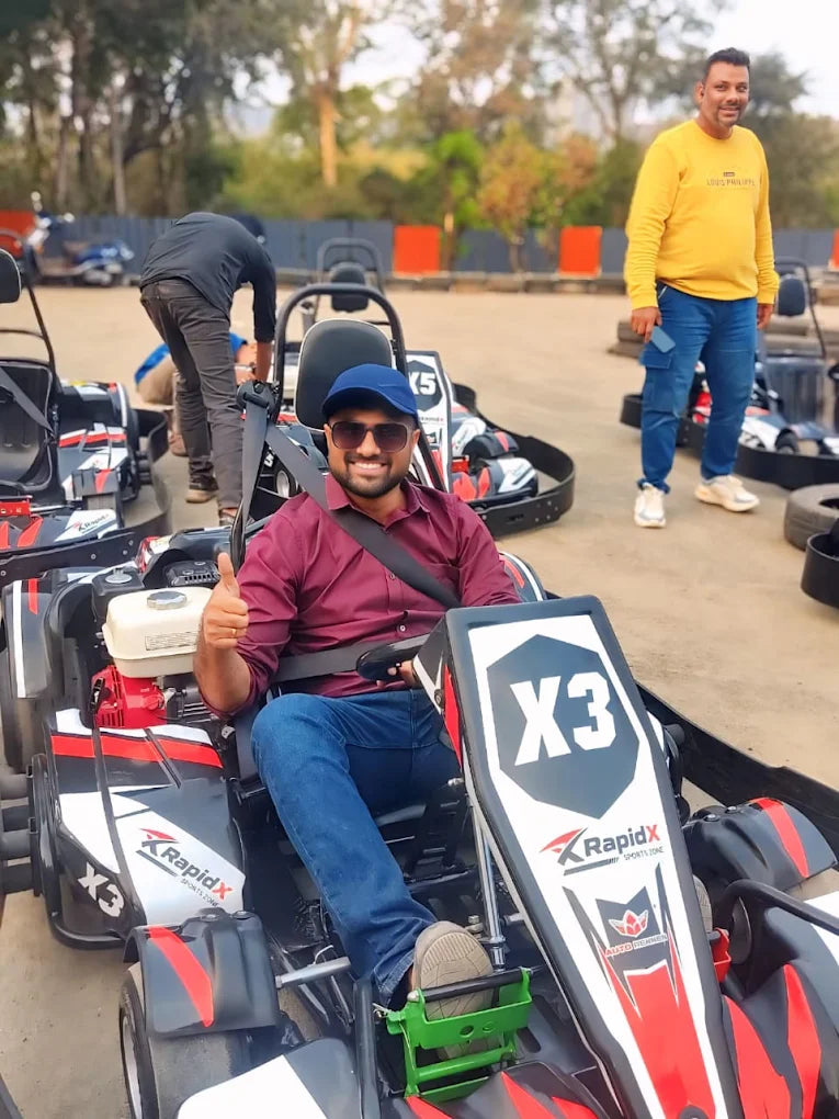 A man in a go-kart gives a thumbs up, while another man stands behind him.