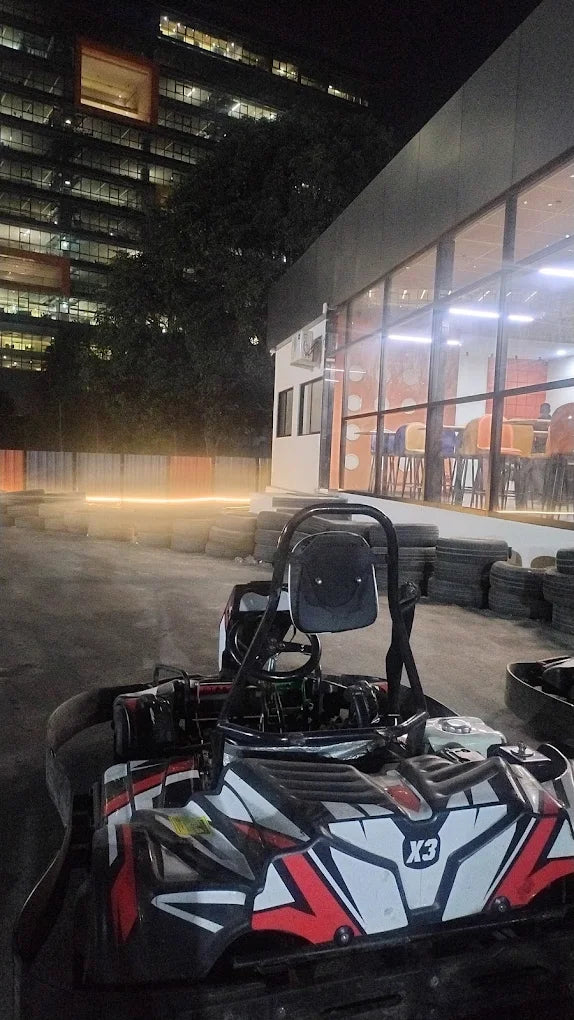 A go-kart sits on a track at night, with a building and lights in the background.
