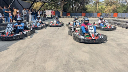 Adults in go-karts on a track, with spectators in the background.