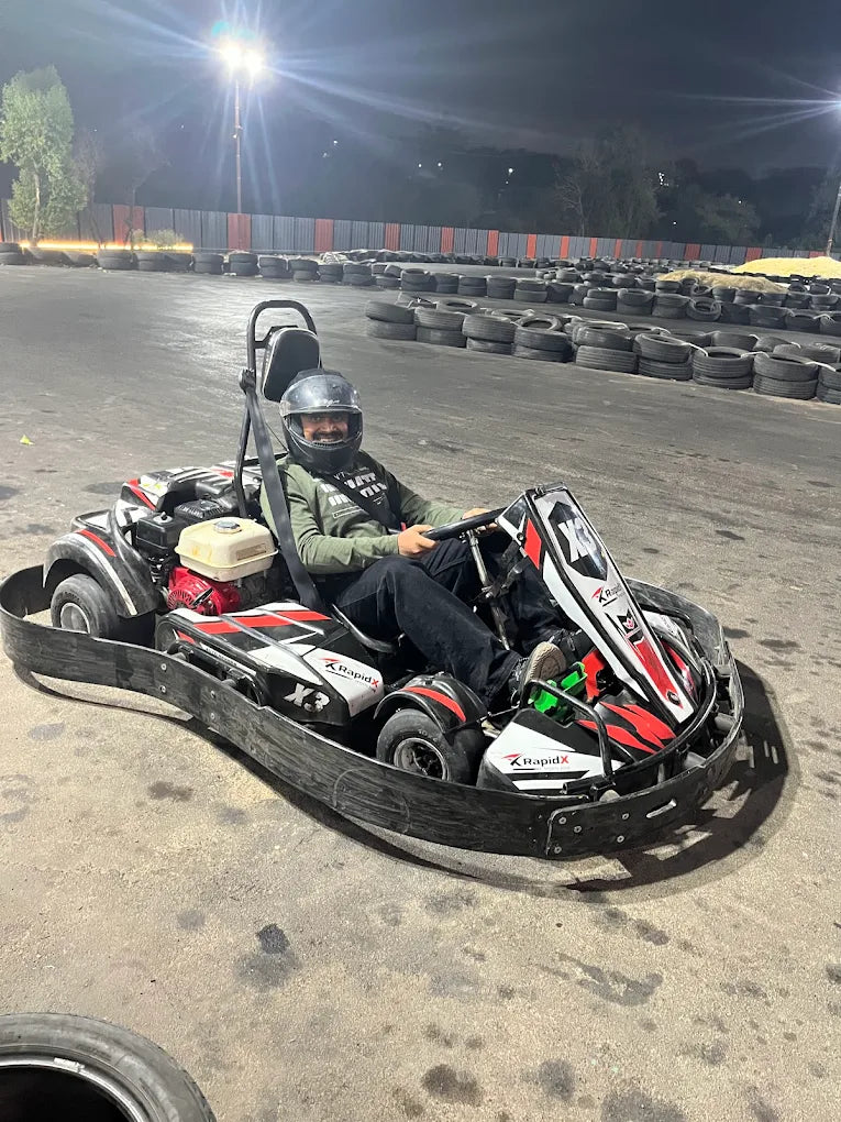 A person in a go-kart at a nighttime track smiles at the camera.
