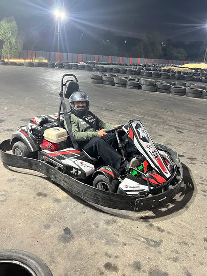 A person in a go-kart at a nighttime track smiles at the camera.