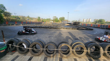 A young person races a go-kart on a track lined with tires, with buildings in the distance.