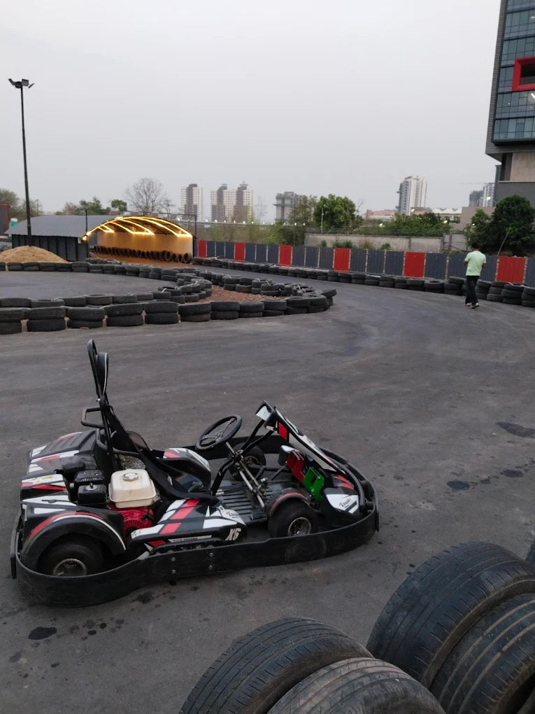 A go-kart sits on a track with a person walking in the background.