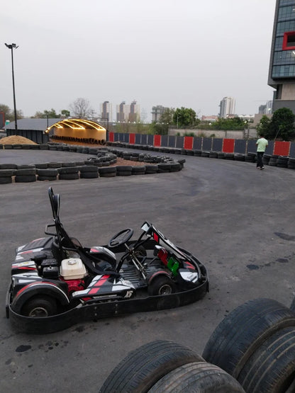 A go-kart sits on a track with a person walking in the background.
