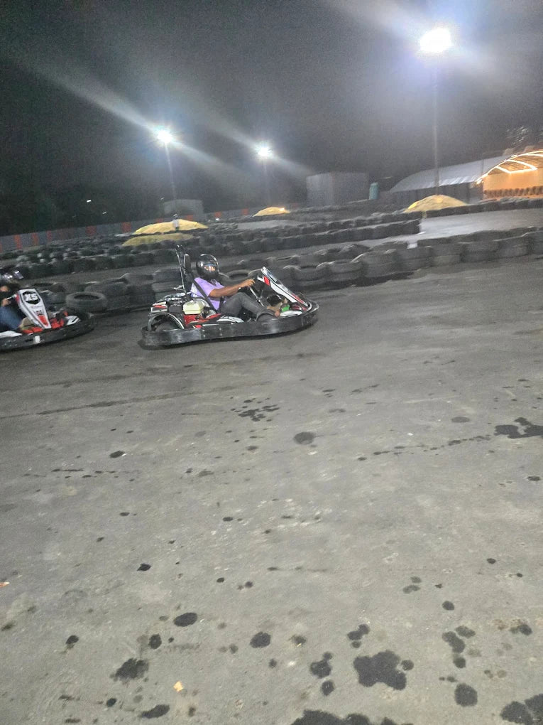 Two people race go-karts at night on a track lined with tires, illuminated by bright lights.