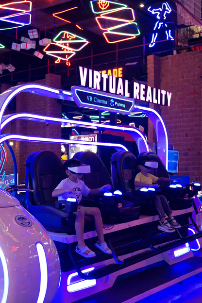 Two children wearing VR headsets sit in arcade chairs, playing a virtual reality game.