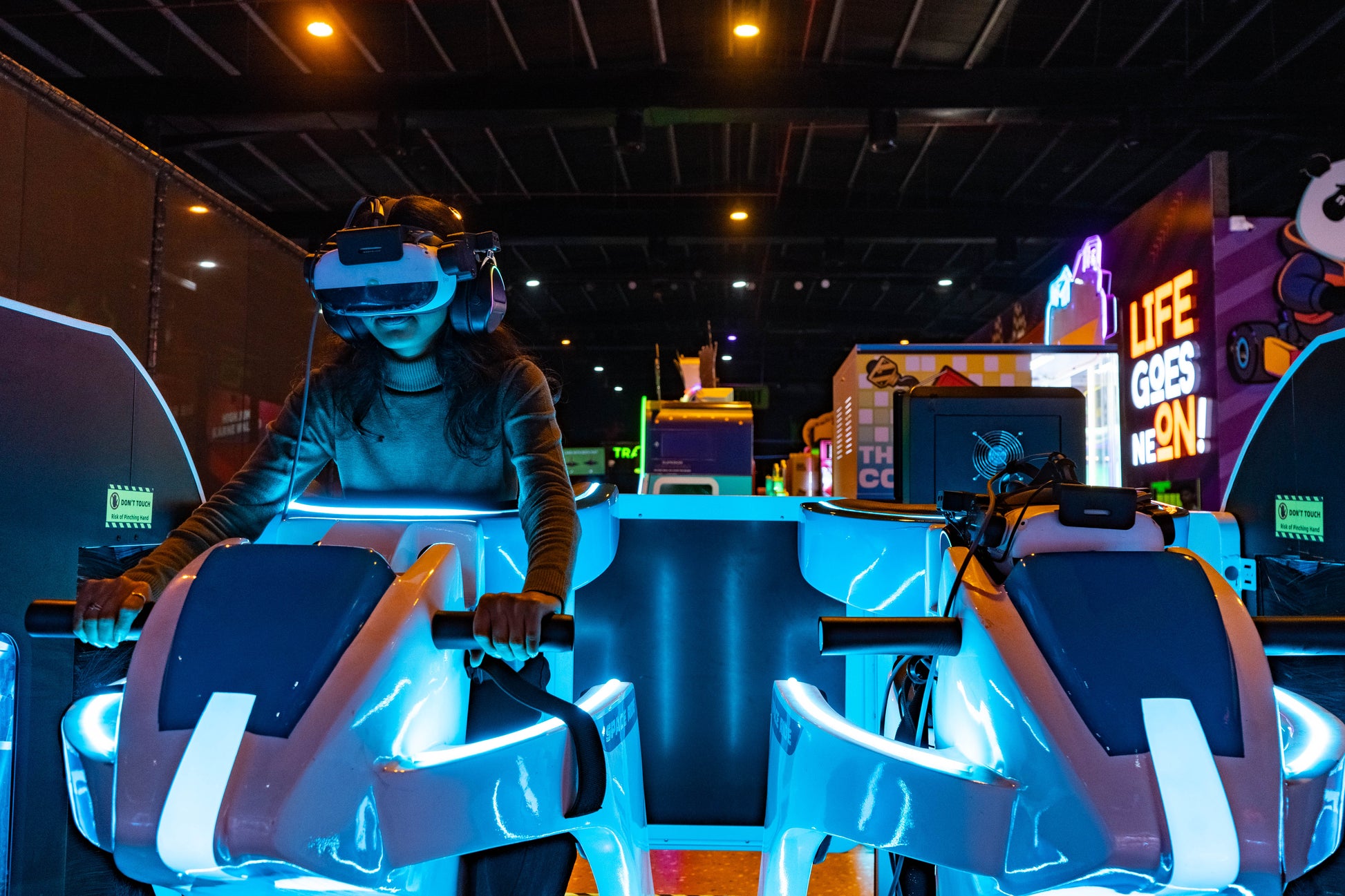 A young person wearing a VR headset plays a racing game in an arcade.