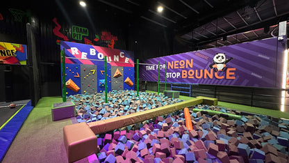 A neon-themed indoor trampoline park with a foam pit, climbing wall, and a panda mascot.