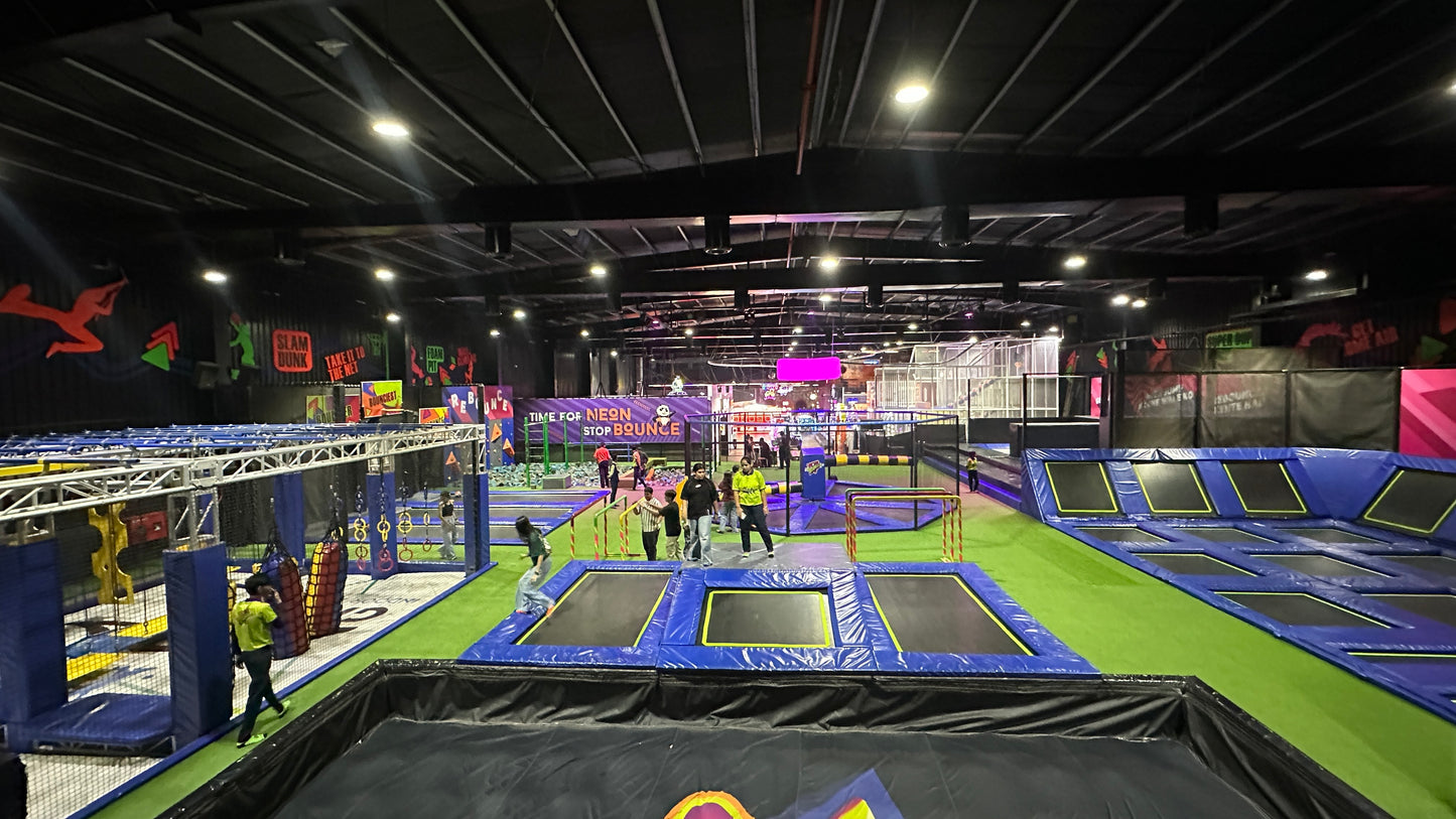 An indoor trampoline park with multiple trampolines and people of various ages enjoying the activities.