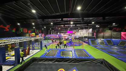 An indoor trampoline park with multiple trampolines and people of various ages enjoying the activities.