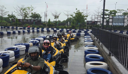 People in go-karts on a wet track, wearing helmets.