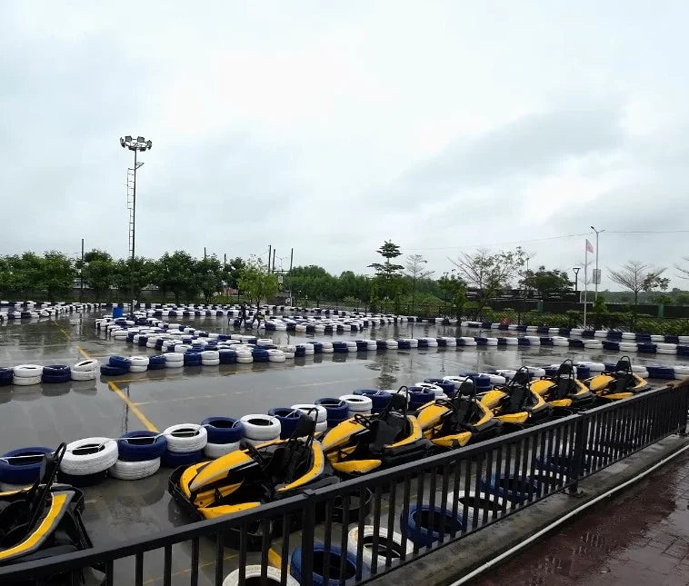 Go-karts lined up on a wet track with tire barriers under a cloudy sky.