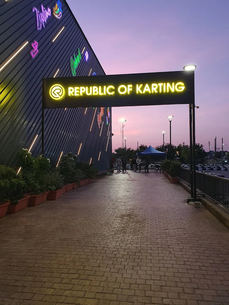 A neon sign reads "Republic of Karting" above a brick pathway leading to a karting track at dusk.