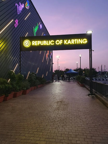 A neon sign reads "Republic of Karting" above a brick pathway leading to a karting track at dusk.