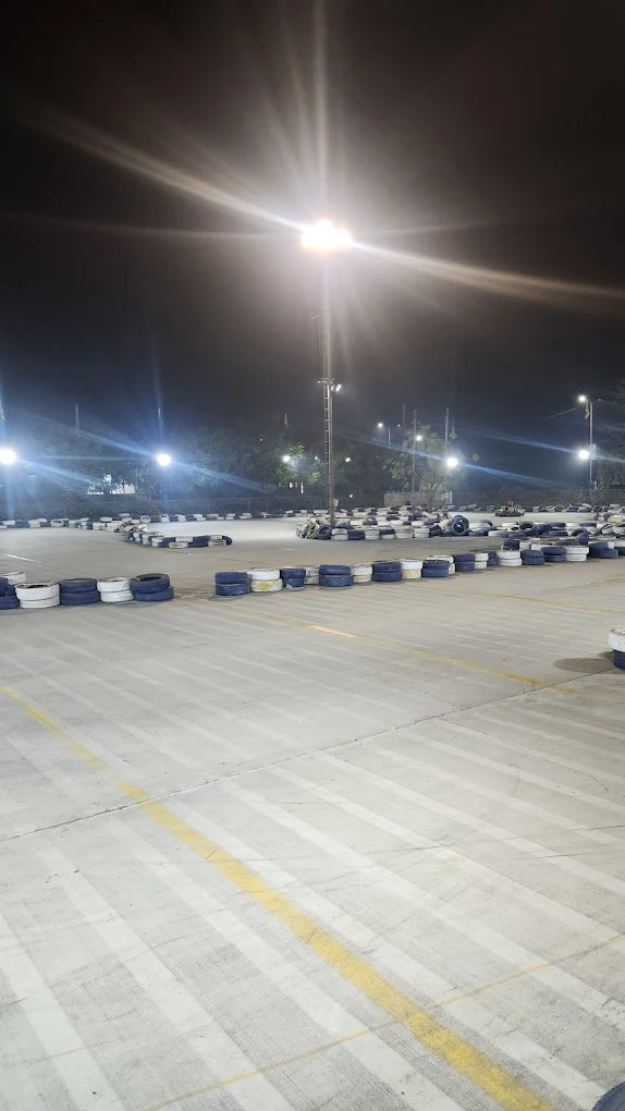 A go-kart track at night, illuminated by bright lights, with tires lining the course.