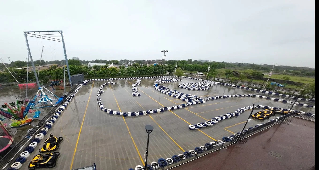 An aerial view of a wet go-kart track with several karts and amusement rides.