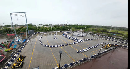 An aerial view of a wet go-kart track with several karts and amusement rides.
