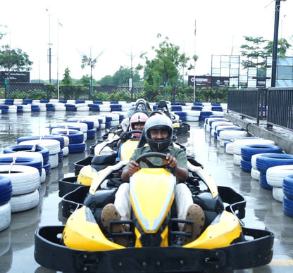 Adults in go-karts on a wet track, wearing helmets and racing.