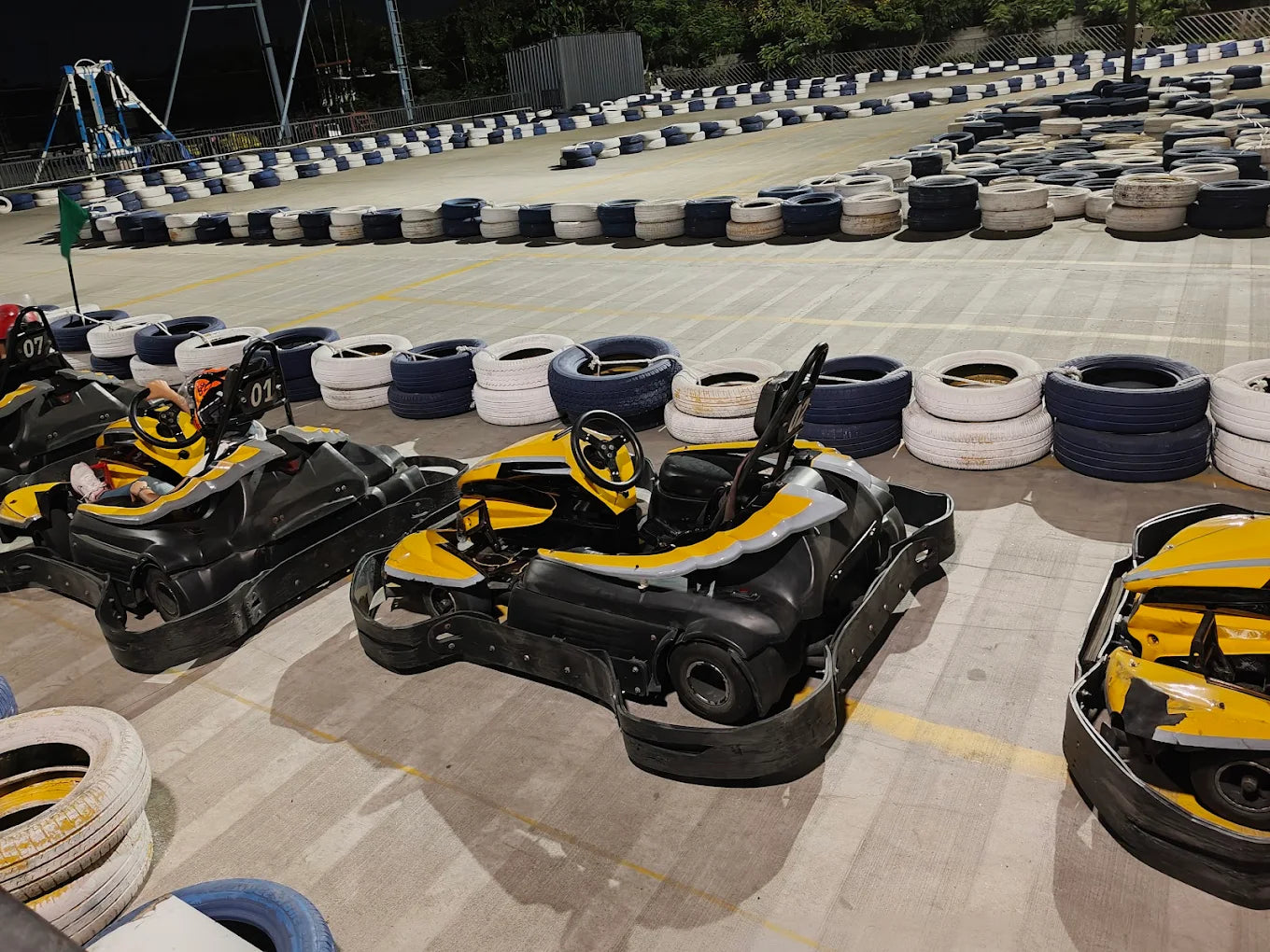 Go-karts are parked on a track with tire barriers, ready for young drivers.