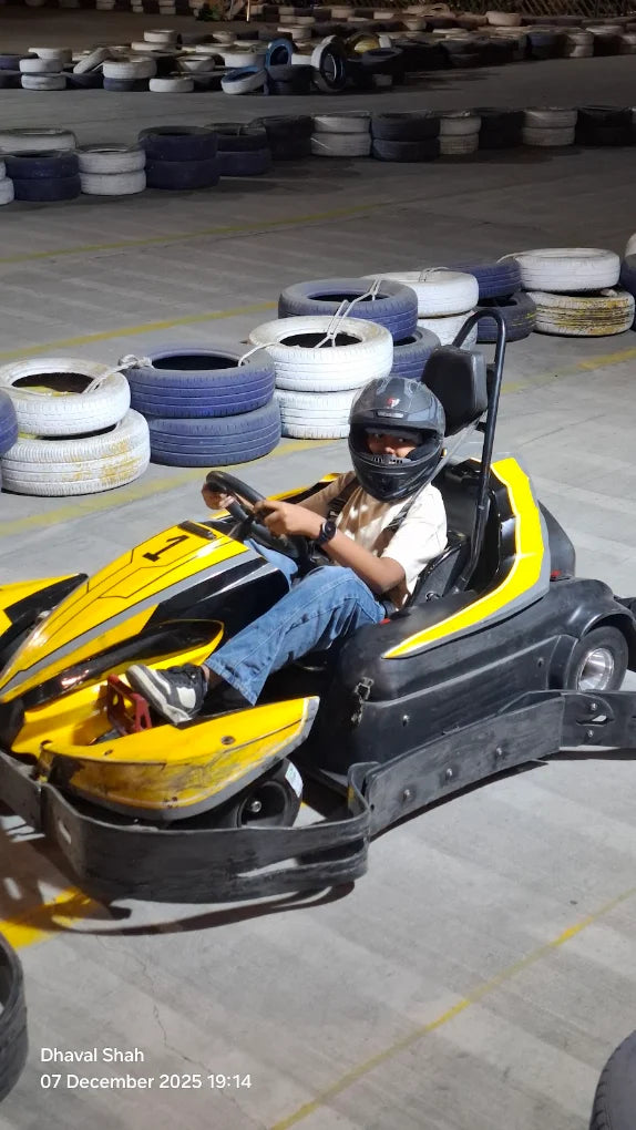 A child in a helmet drives a yellow go-kart on a track surrounded by tires.