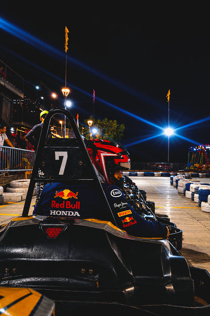 A young person in a racing suit sits in a go-kart at night, ready to race.