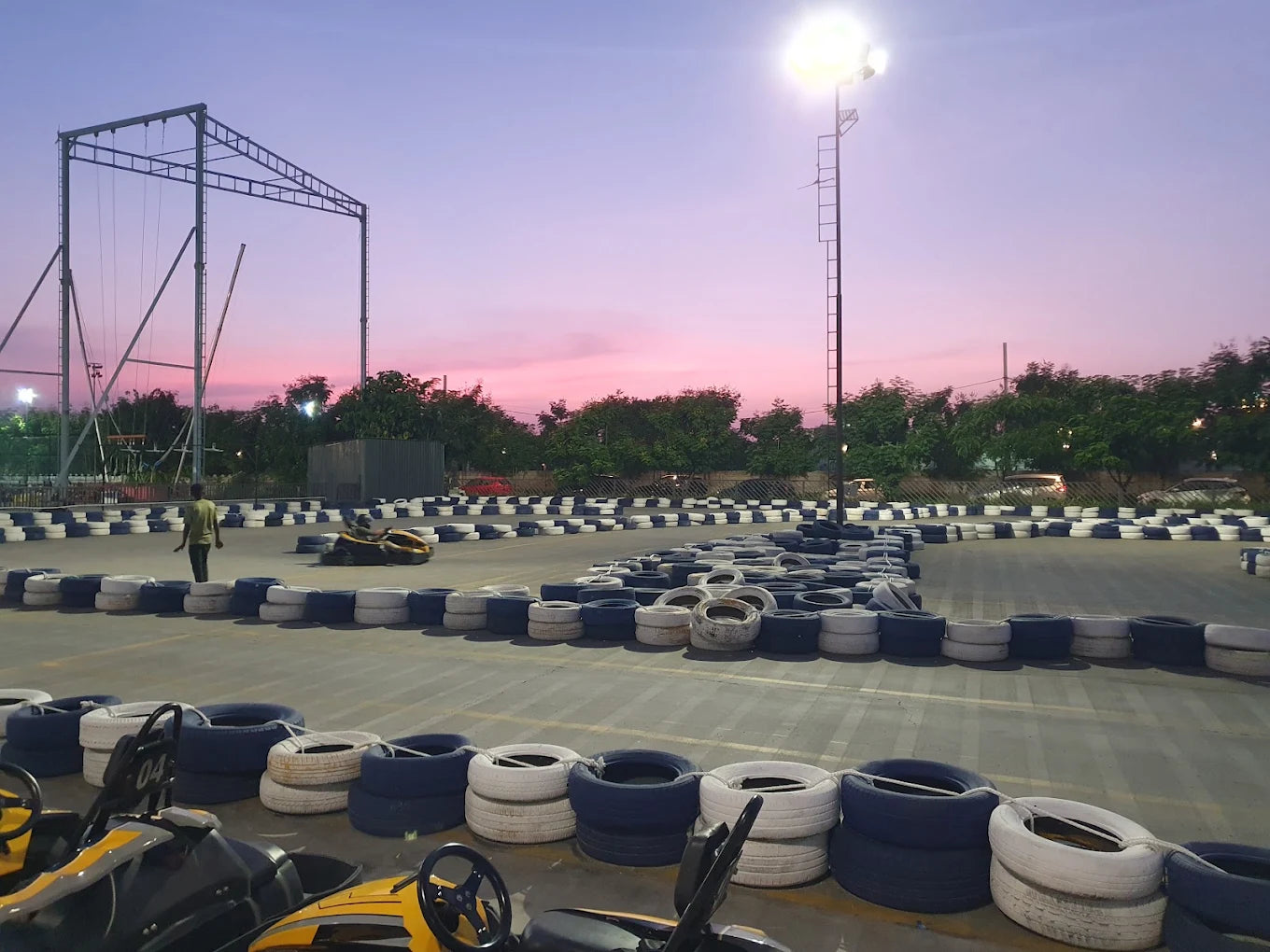 A go-kart track at dusk with a person walking and a go-kart on the track.