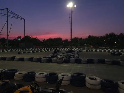 A go-kart track at dusk, with tire barriers lining the course under a colorful sky.