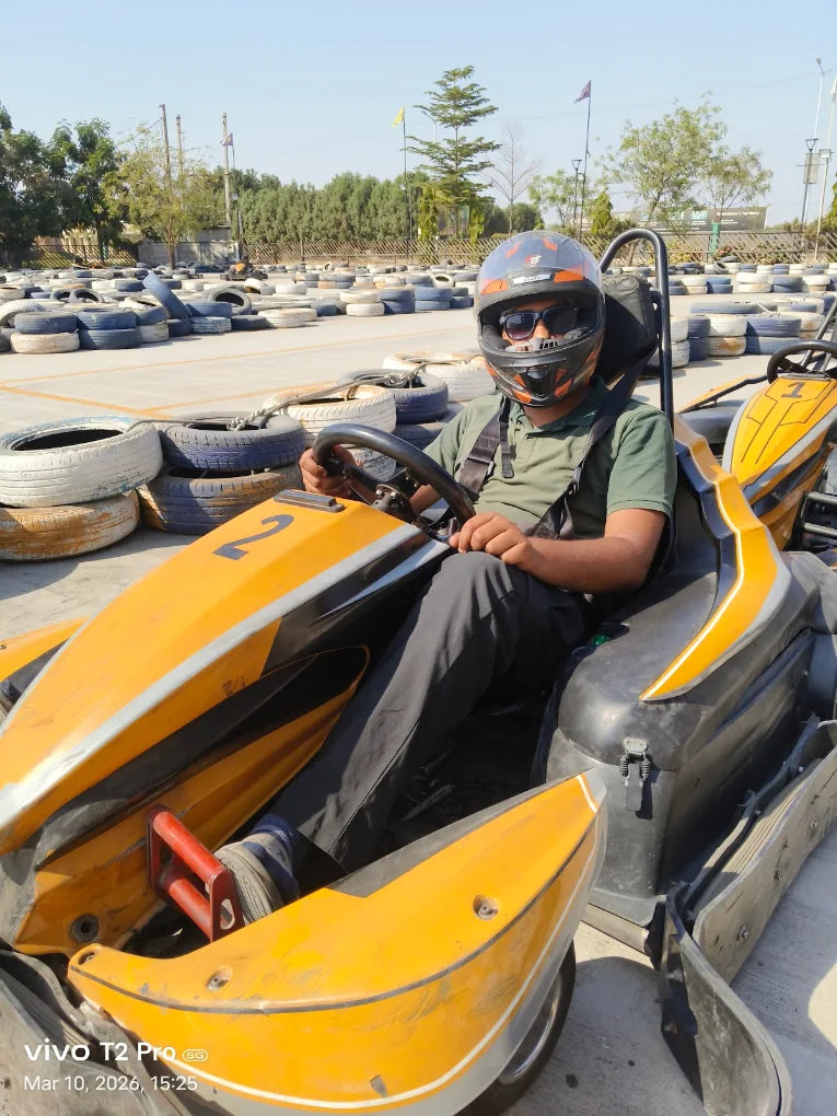 A person in a go-kart helmet and racing suit sits in a go-kart on a track.