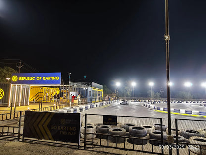 A nighttime go-kart track with bright lights, a building labeled "Republic of Karting," and people enjoying the activity.