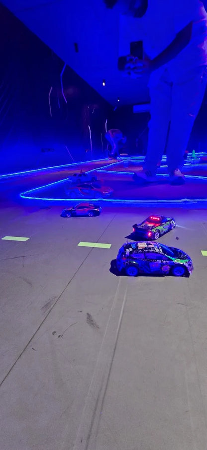 RC cars race on a track lit by blue neon lights, with a person in the background.