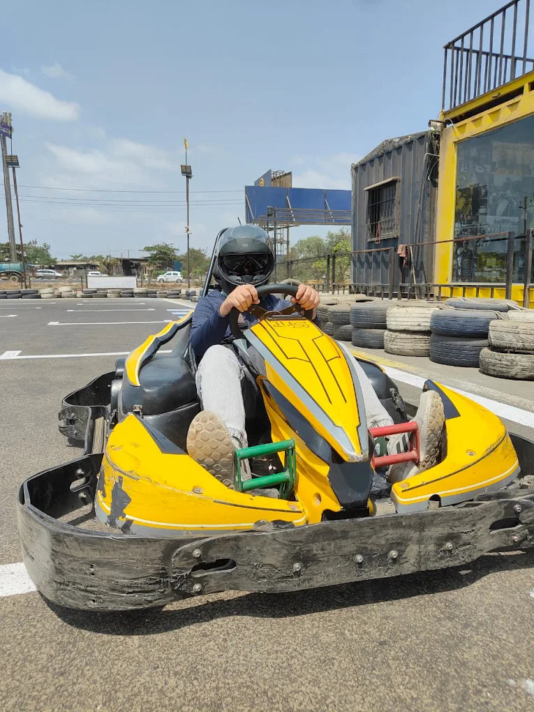 A person in a helmet drives a yellow go-kart on a track.