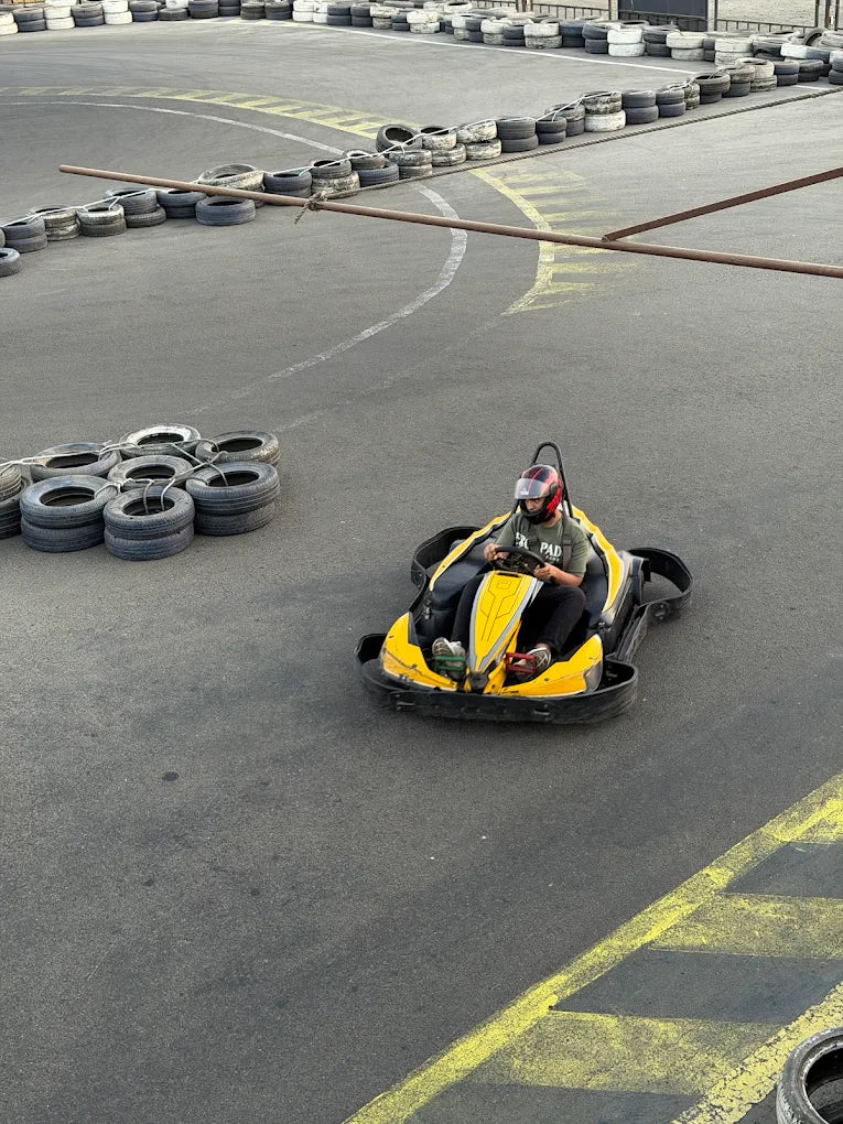 A person in a yellow go-kart wears a helmet and races on a track lined with tires.