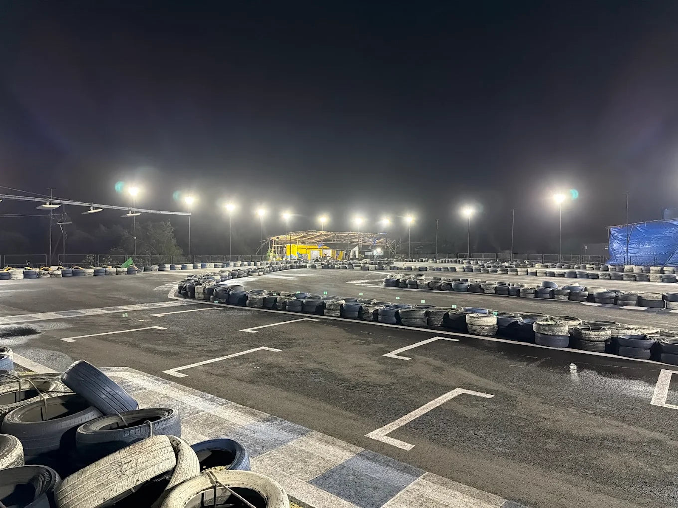 An empty go-kart track at night, illuminated by bright lights, with stacks of tires lining the track.
