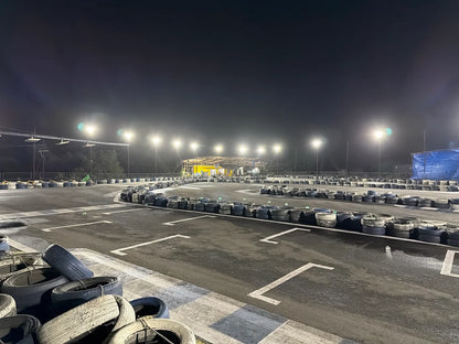 An empty go-kart track at night, illuminated by bright lights, with stacks of tires lining the track.