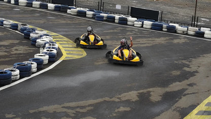 Two people in go-karts race on a track lined with tires.