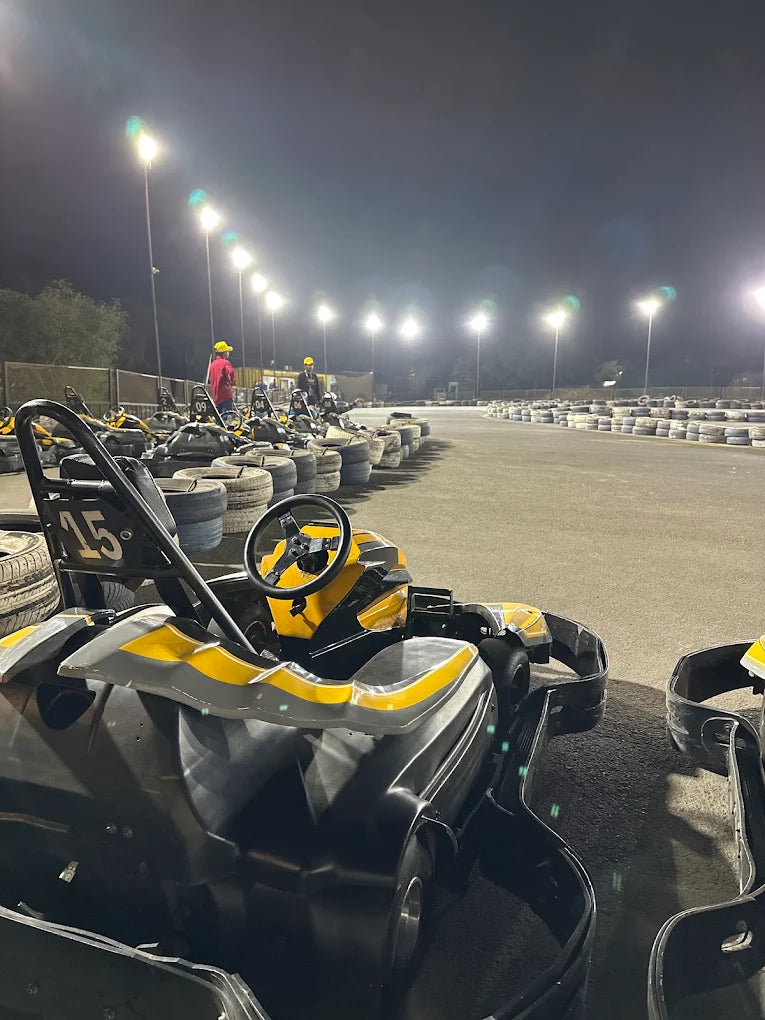 Go-karts lined up at a nighttime track with floodlights and a few people.