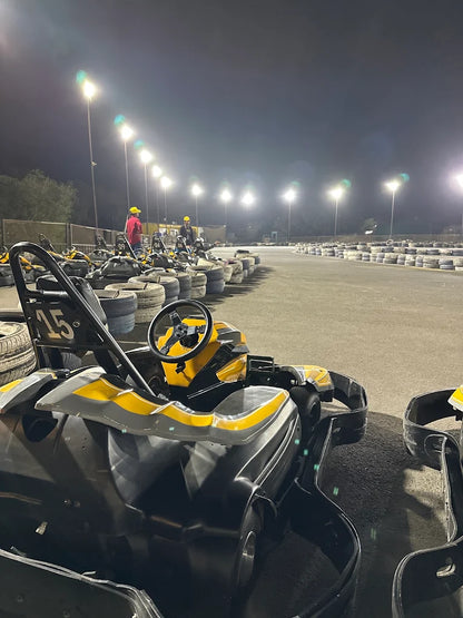 Go-karts lined up at a nighttime track with floodlights and a few people.