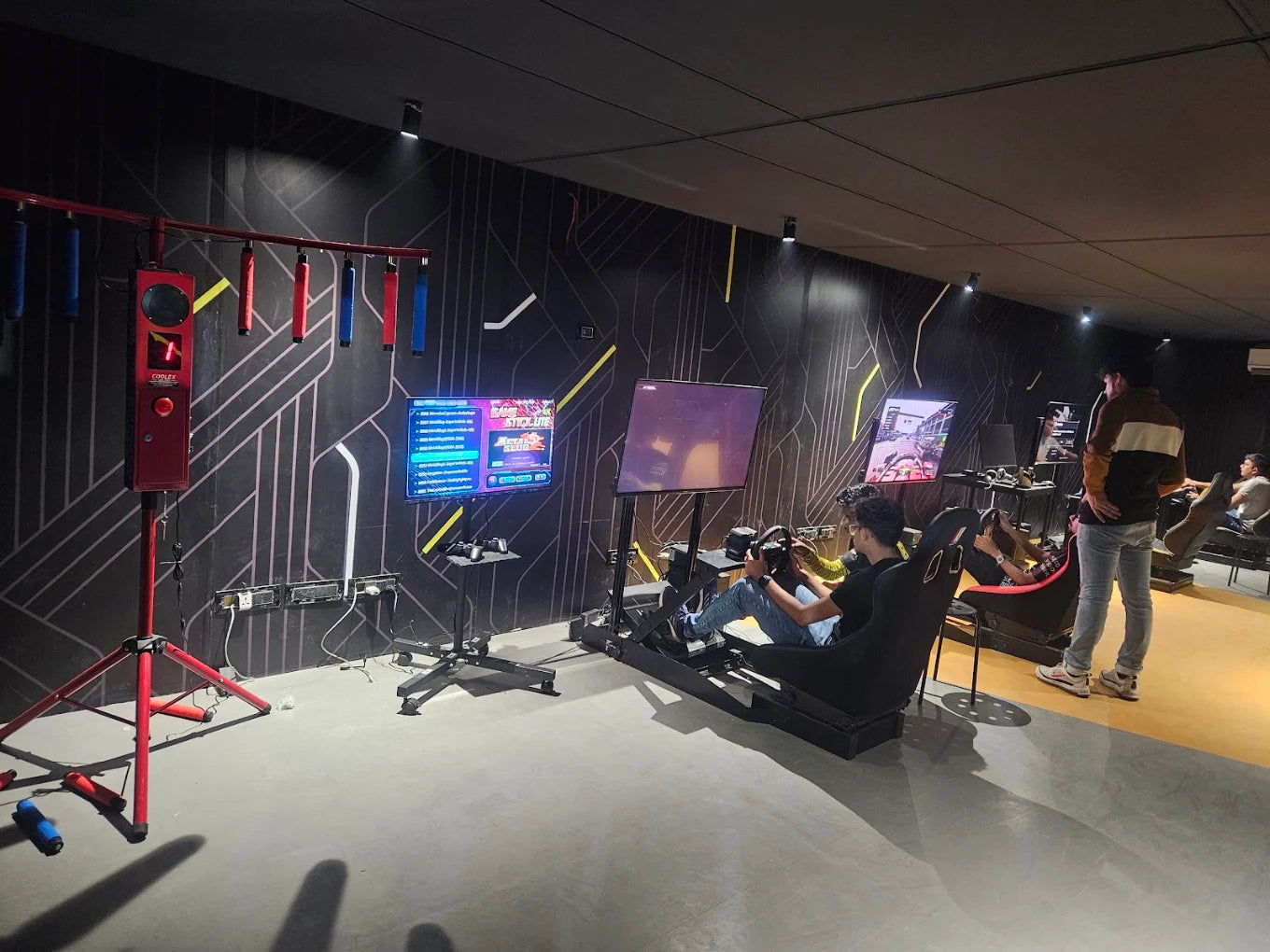 Young adults play racing simulation games in a dimly lit arcade with futuristic decor.