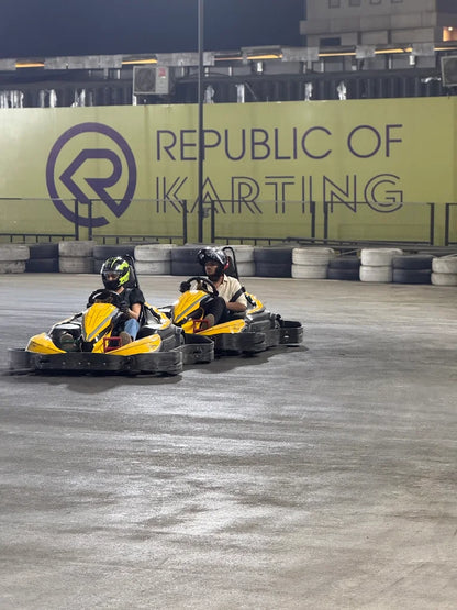 Two young people in go-karts race on a track at night, with a "Republic of Karting" sign in the background.