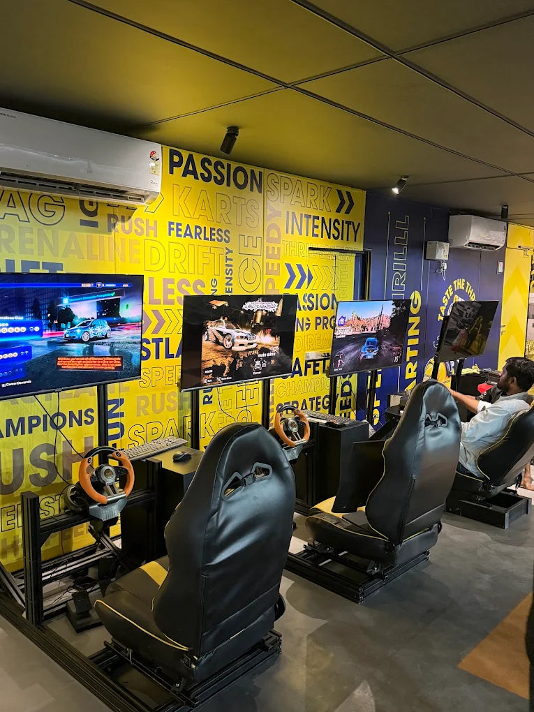 Racing simulators with black and yellow seats and steering wheels in a room with yellow and blue walls.