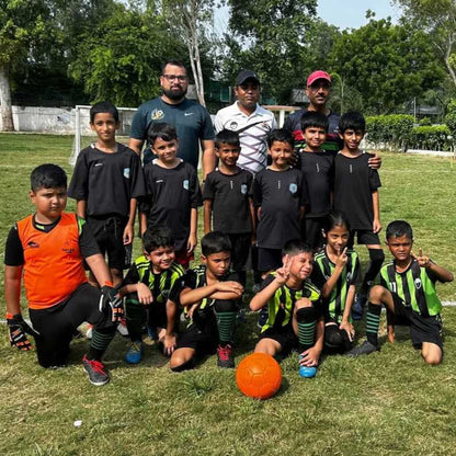 Group of children in sports uniforms with a coach on a grassy field.