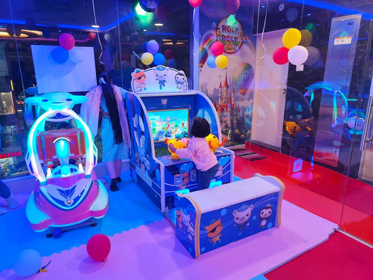 A young child plays an arcade game in a colorful, brightly lit amusement center. A woman stands nearby, observing.
